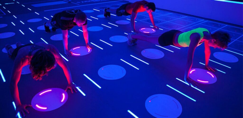 4 pessoas realizam flexões no chão de uma academia iluminado por soluções leds